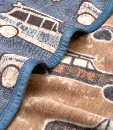 Blue-bound blanket with tan and cream vintage van pattern featuring circular wheels and rectangular wagon details.5