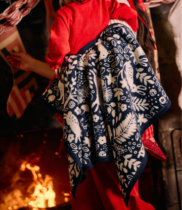 Navy mini blanket with cream botanical and forest animal pattern held by person in red shirt.2