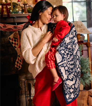 Navy mini blanket with white forest and animal print worn over child's shoulder in holiday setting.5