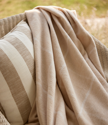 Wheat-colored lightweight blanket with cream windowpane stripe draped over wicker chair.3