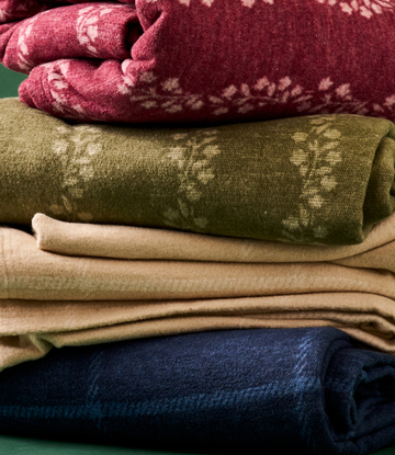 Stacked folded blankets in burgundy, olive, beige, and navy with windowpane woven patterns.3