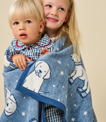 Blue knit blanket with white puppy and snowflake pattern, shown wrapped around two young children.6
