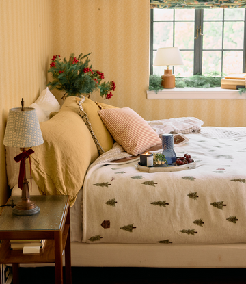 Cream blanket with small green tree pattern draped across a bed with yellow pillows and bedding.3