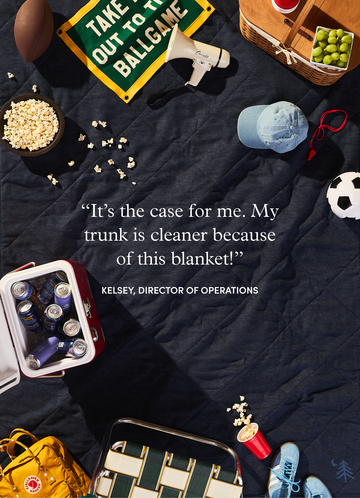Dark navy quilted blanket displayed with sports equipment, snacks, cooler, and picnic items arranged around it.6