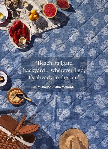 Blue outdoor blanket with white floral pattern, displayed with picnic food and accessories from overhead view.7