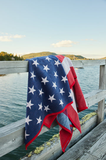 Blue and red striped blanket with white stars draped over a wooden dock railing overlooking water.7