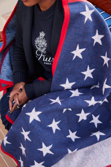 Navy blanket with white stars and red trim draped over a person's shoulders.4